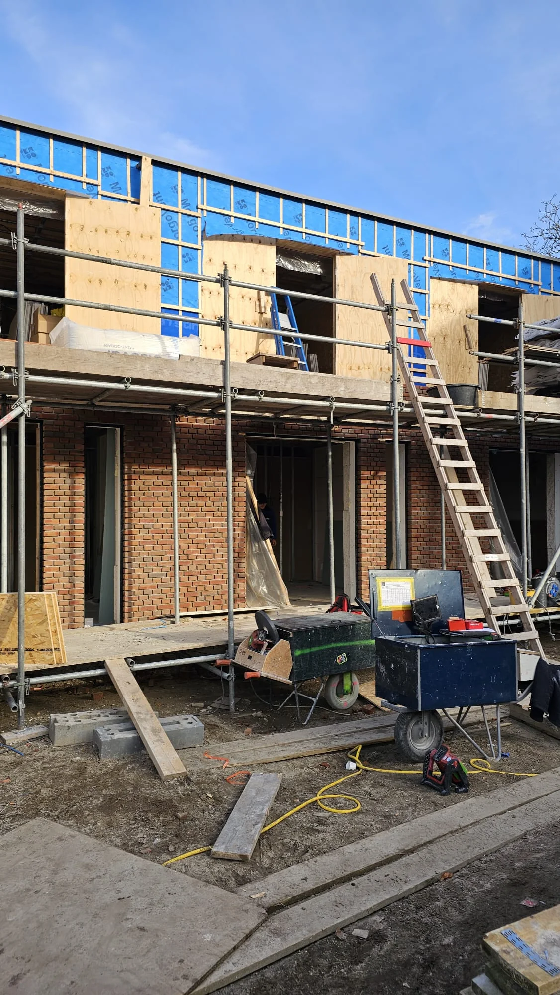 Rijwoningen in aanbouw met metselwerk, houten gevelplaten en steigers